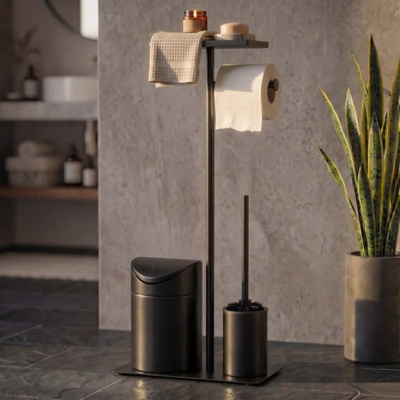 Set de baño negro mate ante una pared de piedra, con una toalla, una vela y una jabonera en la bandeja y una planta al lado
